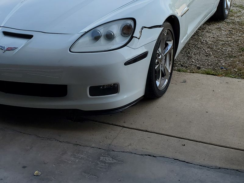 A white Chevrolet Corvette with the front bumper cover split and pulled away from the fender.