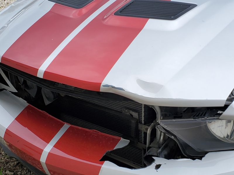 A white Ford Mustang with red stripes, the front end damaged in a collision.