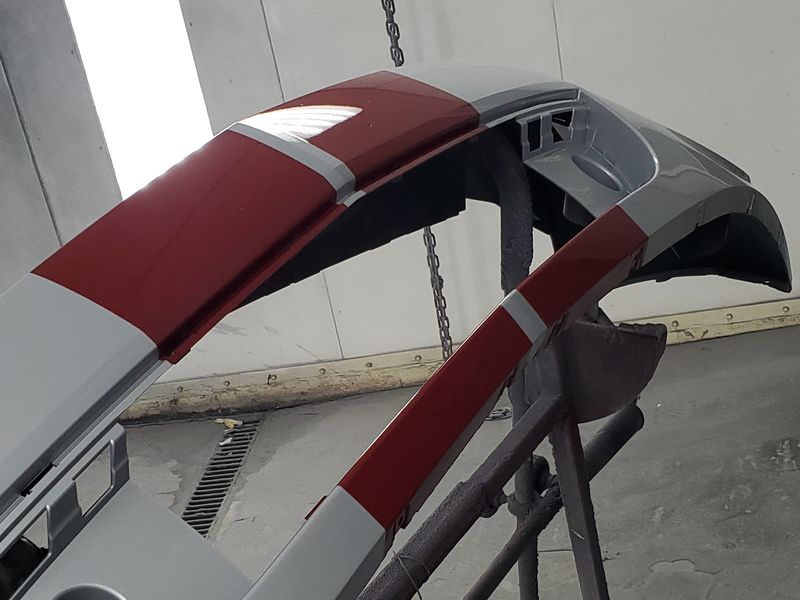 The Mustang's front bumper cover on a rack, refinished in white with the red stripe laid back in.