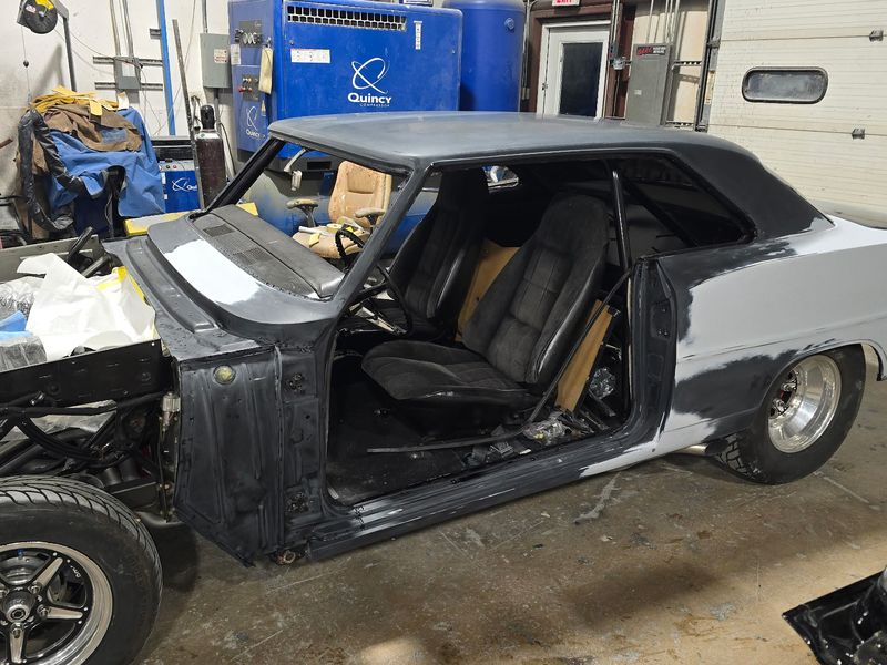 The Chevrolet Nova stripped to bare panels and primer with the doors and glass out.